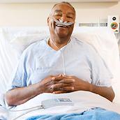 Smiling patient with Hillrom Life2000 mobile ventilator talking with doctor or respiratory therapist in hospital hallway.