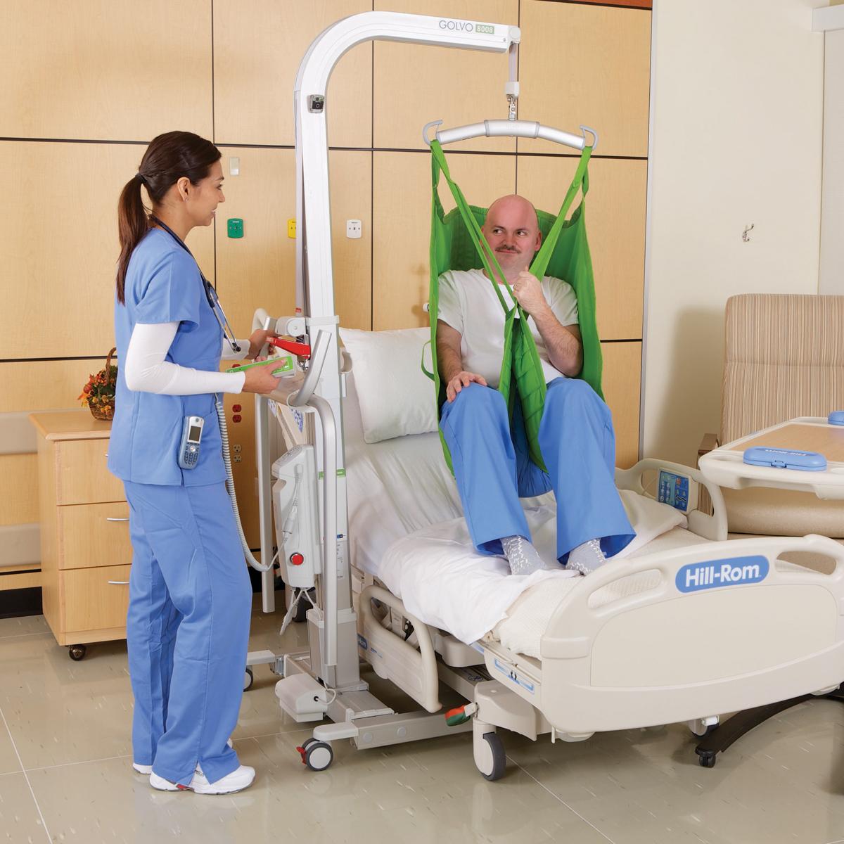 En patient lyfts ovanför en sjukhussäng med en Golvo mobillyft som används av en kliniker