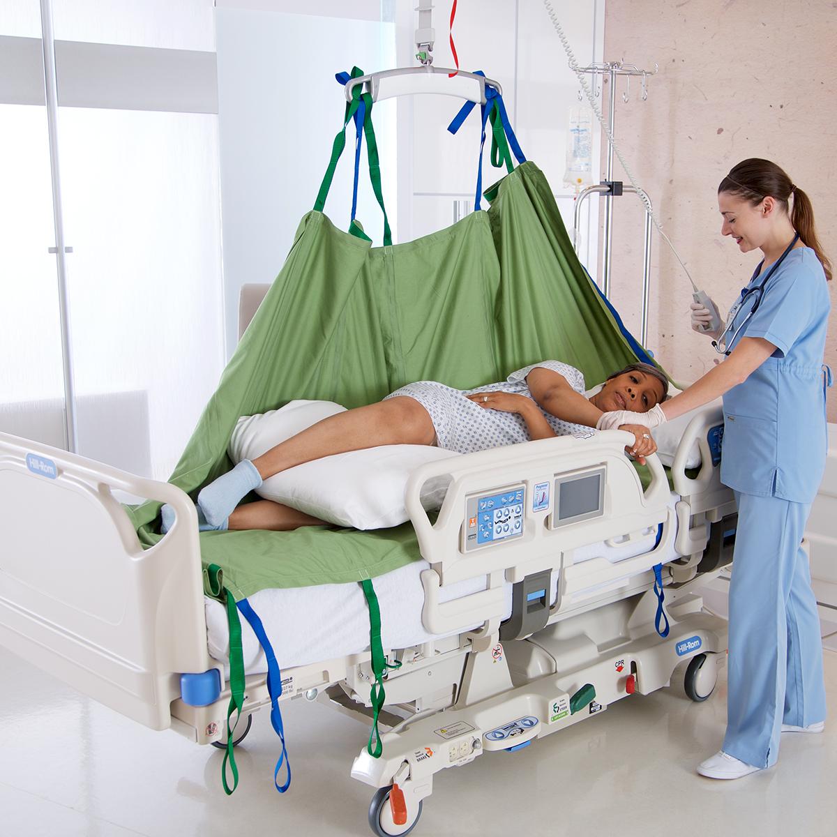 ผู้ดูแลใช้เครื่องยกเหนือศีรษะและ Repo Sheet ของ Hillrom เพื่อจัดเปลี่ยนท่าให้ผู้ป่วยที่นอนอยู่บนเตียง