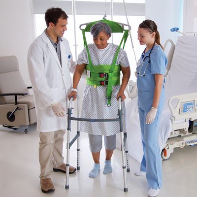  An overhead lift attached to a green vest supports a female patient using a walker, with two clinicians helping