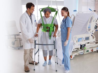 A clinician helps a patient stand using a mobile patient lift from Baxter.