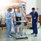 A patient is safely supported by his clinicians and a Viking XL mobile lift while exiting a TotalCare Bariatric Plus Hospital Bed.