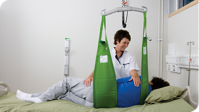 Healthcare worker using a LIKO patient lift with green sling to reposition a patient in a hospital bed.