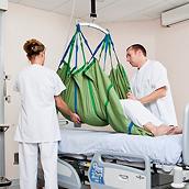 Twee artsen gebruiken een Hillrom-plafondlift en Repo Sheet om een patiënt boven een ziekenhuisbed te plaatsen