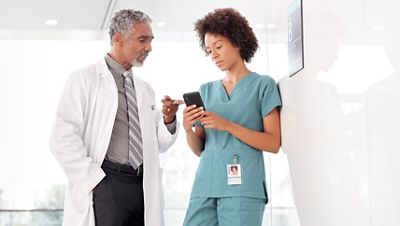 Two clinicians talk while referencing data on a smartphone
