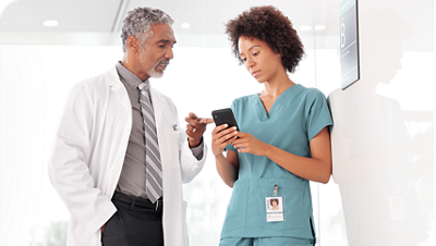 A doctor and a nurse review information together on a smartphone in a clinical hallway.