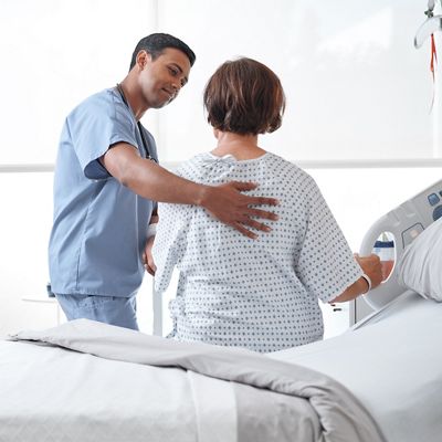 Nurse resting his hand on the back of a patient sitting on a hospital bed