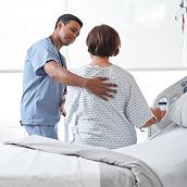 Sjuksköterska som lägger handen på ryggen på en patient som sitter på en sjukhussäng