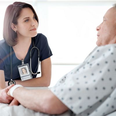 A clinician listens to her patient, who is lying in a hospital bed.