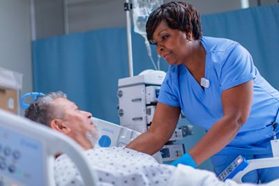 A clinician helps a patient lying in a Med-Surg hospital bed.