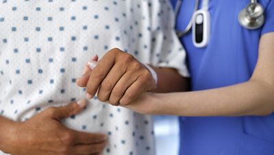 A clinician supports a patient’s arm and back while standing