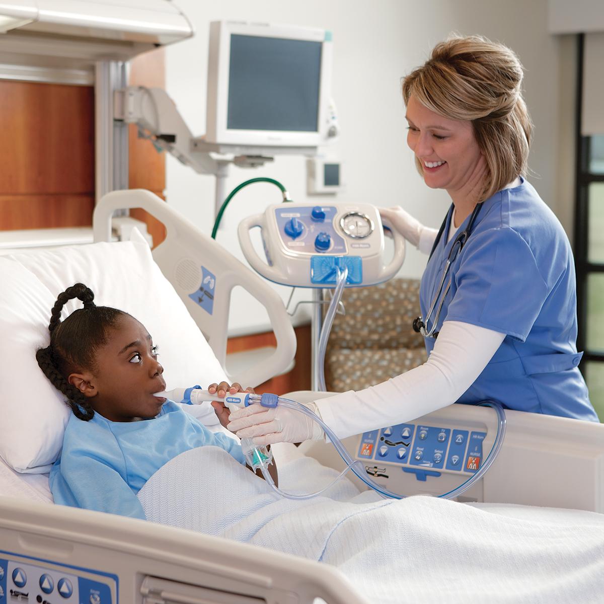 A young patient in a hospital bed receives therapy from the MetaNeb system, with help from her clinician