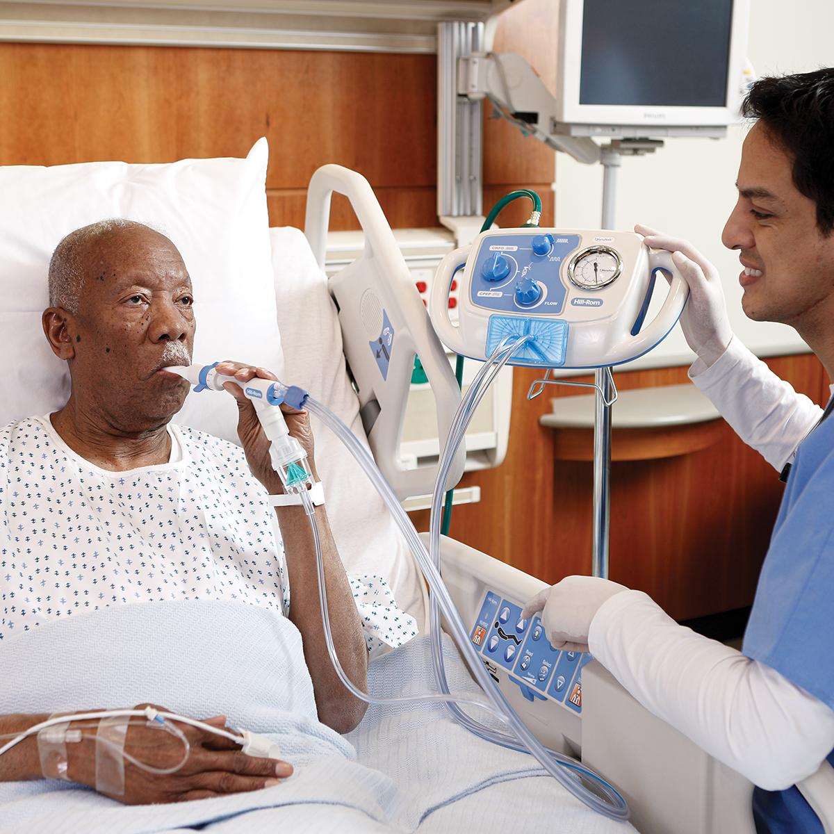 Um paciente mais velho em uma cama hospitalar recebe terapia do sistema MetaNeb, com o médico próximo