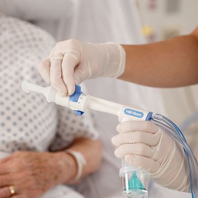 A clinician with a gloved hand adjusts the MetaNeb Circuit, patient in background