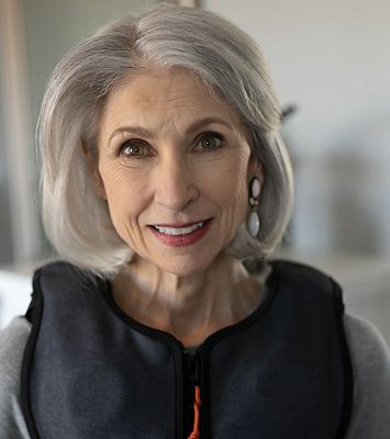 A smiling woman wears her Monarch vest for respiratory therapy at home.