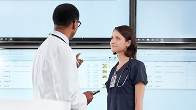 A nurse and physician looking at the Voalte Status Board to see real-time, unit-level visibility of patient information, active alerts, and staffing assignments