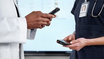 Two clinicians read information on their smartphones in a hospital hallway