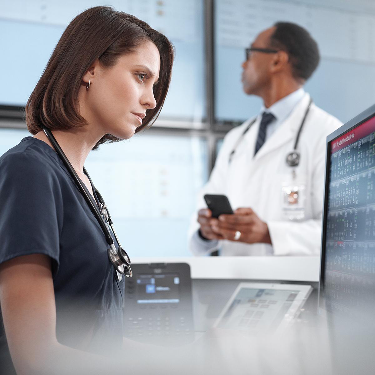 Nurse using Connex Central Station on desktop computer, doctor in background using smartphone