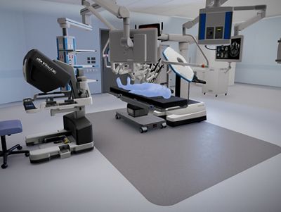 A clinician stands in front of an inclined surgical table with stirrups in a robotic operating room