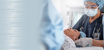 A patient wearing a nasal cannula lays flat on a Hillrom surgical table while her surgeon is wearing a mask and goggles