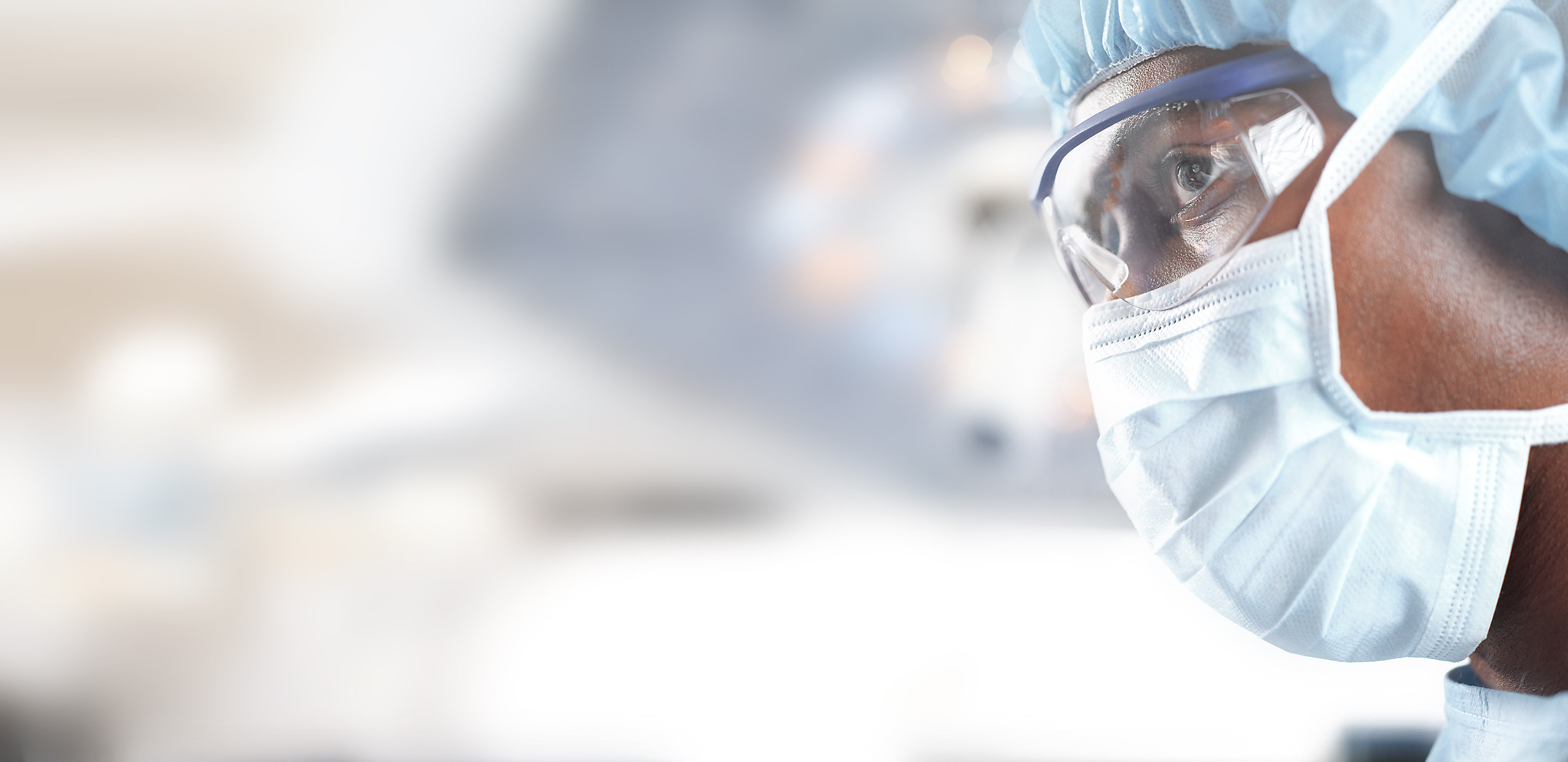 Imagem aproximada de um membro da equipe cirúrgica durante a cirurgia, foco cirúrgico Hillrom em segundo plano.