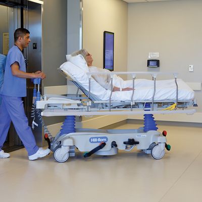 A clinician pushes a Hillrom Procedural Stretcher carrying a patient out of a hospital elevator. 