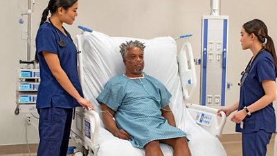 A patient sits in a Progressa+ bed in FullChair position with two clinicians nearby