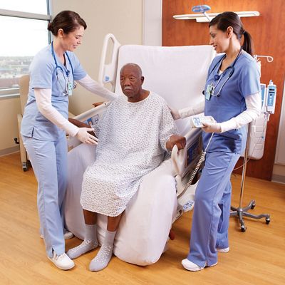 Progressa Bed in sitting position, with two female clinicians helping elderly male patient in sitting position