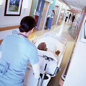 プログレッサベッドシステムに横たわる男性患者と、病院の廊下を搬送する女性医師（背後からの画像）
