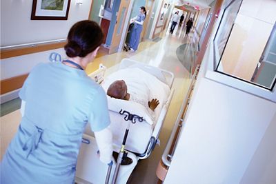 A clinician transports a patient in a Progressa bed down a hospital corridor
