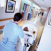 A clinician transports a patient in a Progressa bed down a hospital corridor