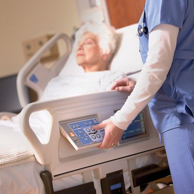 Elderly female patient lies in Progressa bed while female clinician uses bed controls