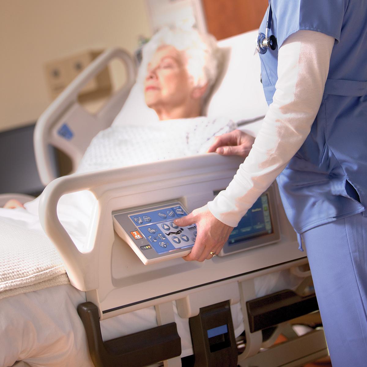 A patient lies in a Progressa bed while her clinician uses the bed controls.