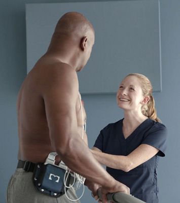 A clinician speaks with a patient on a treadmill before a cardiac stress exam.
