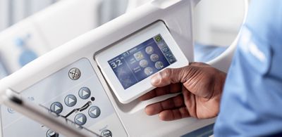 A Hillrom service technician holds a tablet while inspecting a Centrella® Smart+ Bed