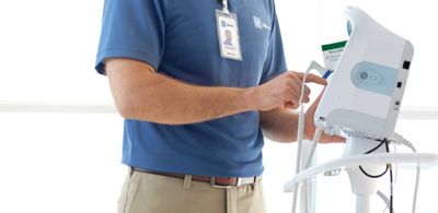 Un técnico de servicio de Hillrom trabaja en un monitor de signos vitales Connex® en una sala de hospital. También se puede ver una cama Centrella® Smart+.