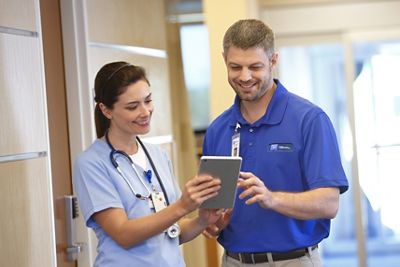 Infirmière et technicien de Hillrom qui discutent avec une tablette dans les mains