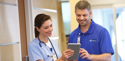 A Hillrom support representative looks at a tablet with a clinician in a hospital corridor