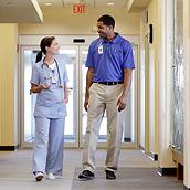A clinician and a Hillrom support professional chat as they walk in a healthcare facility corridor.