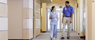 Un instructeur Hillrom et un médecin marchent dans un couloir d'hôpital en discutant