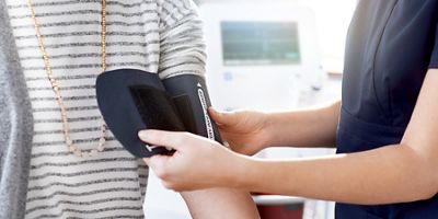 Clinician places a blood pressure cuff on a patient’s bare arm.