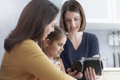 A young girl, her mom and a nurse smile after a vision screening with the Spot Vision Screener