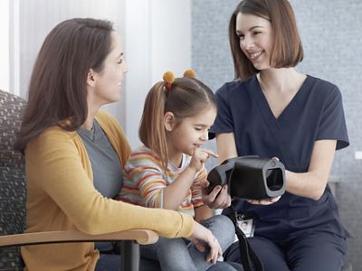 nurse with child and mother looking at spot vision screener device