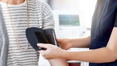 A clinician fastens a blood pressure cuff to a patient’s arm with the Welch Allyn® Spot® Vital Signs device in the background.