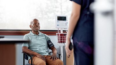 A smiling clinician listens to her patient while sending his vitals to the practice's EMR. The BP cuff on his arm connects to the Welch Allyn Spot Vital Signs 4400 Device.