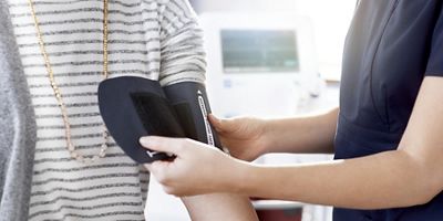 A blood pressure cuff is placed on the arm of a female patient in primary care environment