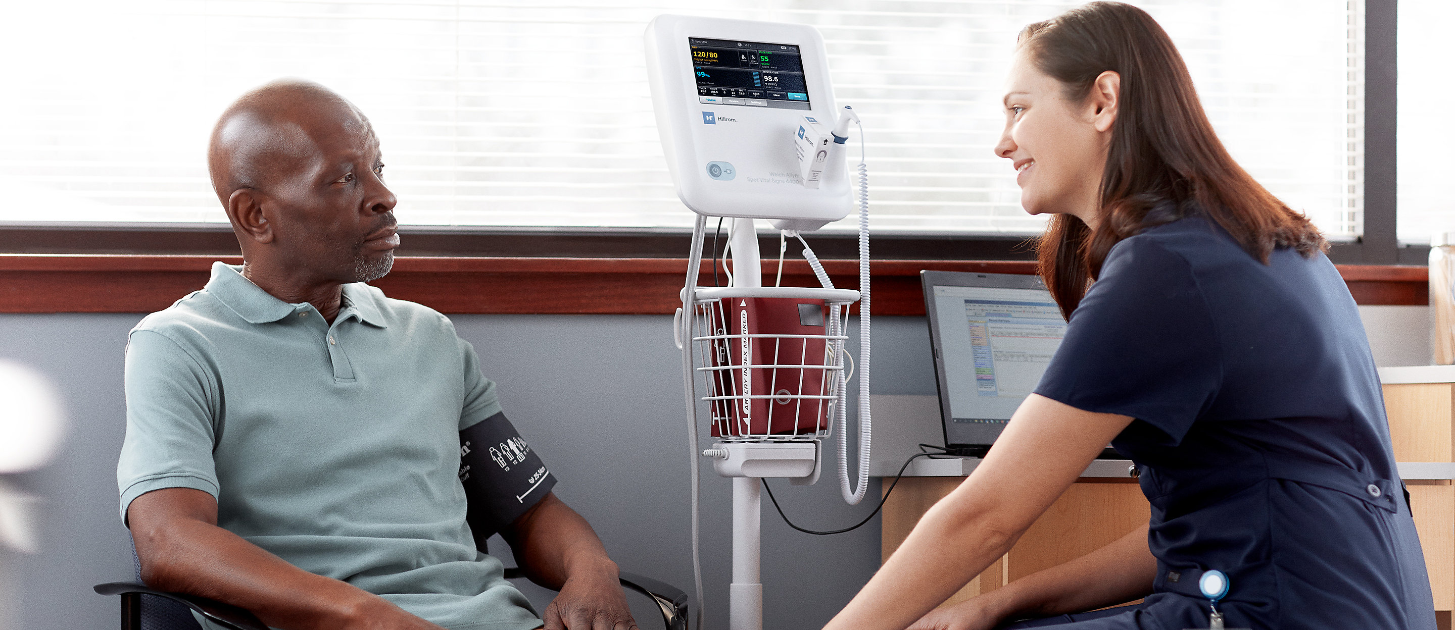 Caregiver rests hand on the knee of a patient with the Welch Allyn Spot Vital Signs 4400 Device in-use