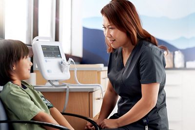 boy sitting in chair with nurse and vital signs monitor