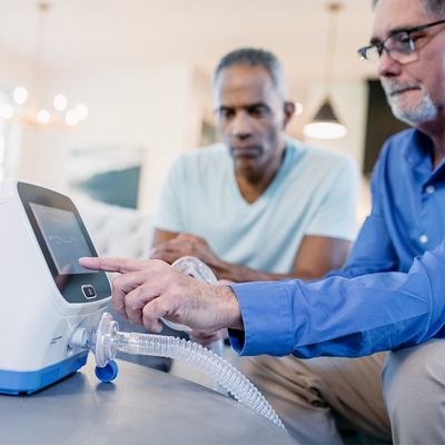 Two men sitting in a living room interact with the Synclara controller.