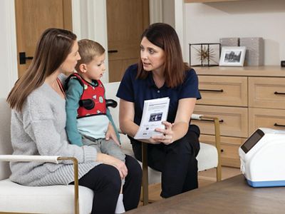 : Image of a CARE CONNEX team member showing a mother and her son, who is wearing the vest garment, how to properly use the system